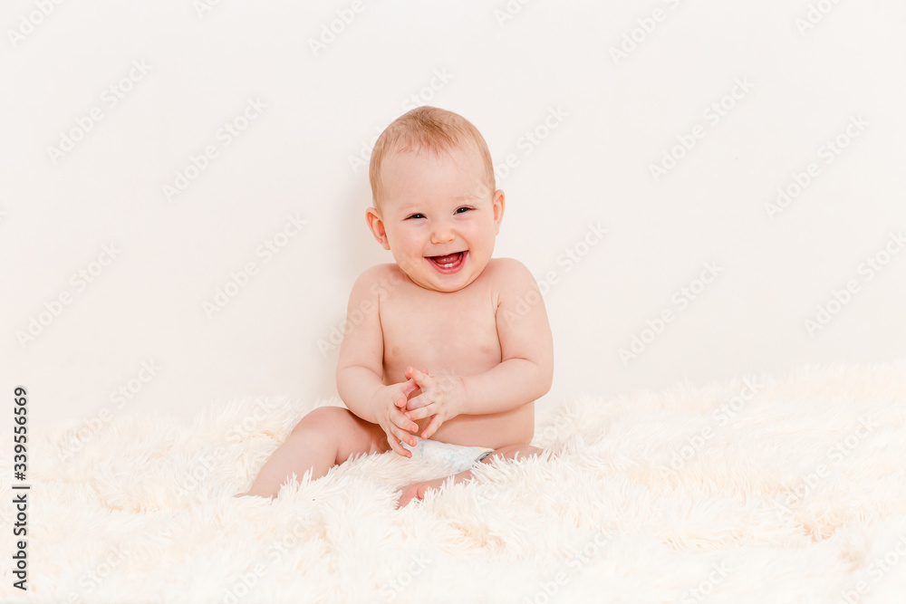 a Caucasian smiling baby girl claps her hands while sitting on the bed at home. baby in one diaper. a Caucasian smiling baby girl claps her hands while sitting on the bed at home. baby in one diaper.
