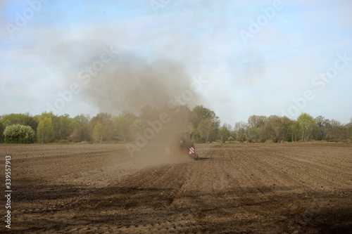 Traktor mit Pflug auf, durch Dürre / Trockenheit, staubigen Acker vom Betrachter wegfahrend photo