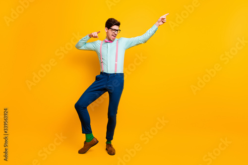 Full length photo of cool stylish guy boyfriend dancing festive mood excited direct finger side wear specs shirt bow tie suspenders trousers shoes isolated vivid yellow color background © deagreez