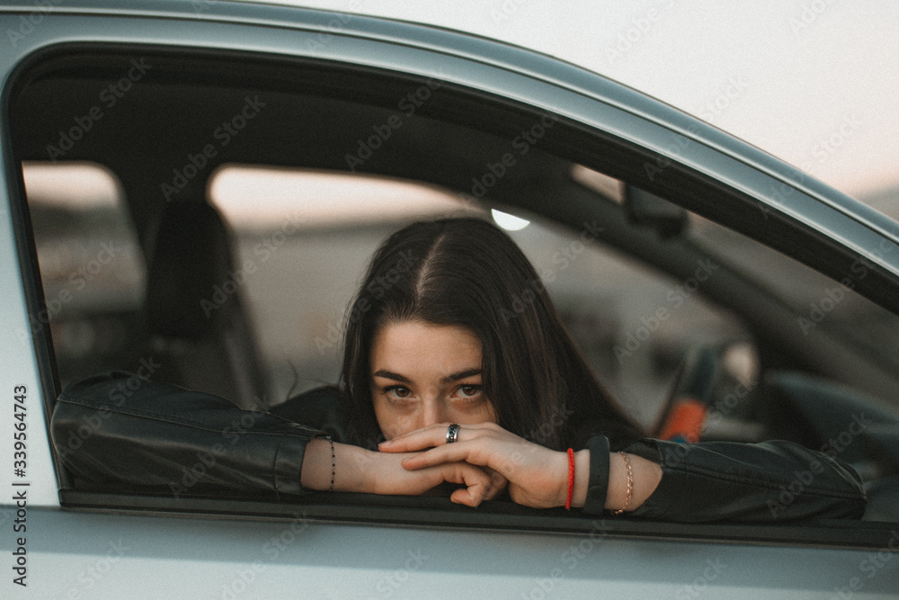 A young woman leaning against the window of a gray car A young woman leaning against the window of a gray car
