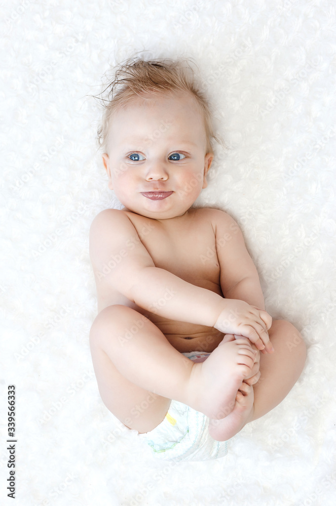 Baby boy of 6 months. Boy holds his legs and looking at camera lying on the bed in the bedroom. Baby boy of 6 months. Boy holds his legs and looking at camera lying on the bed in the bedroom.