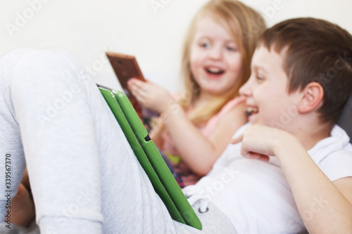 kids with tablet and smartphones in bed at home. Distance learning online education. children playing with gadgets.
