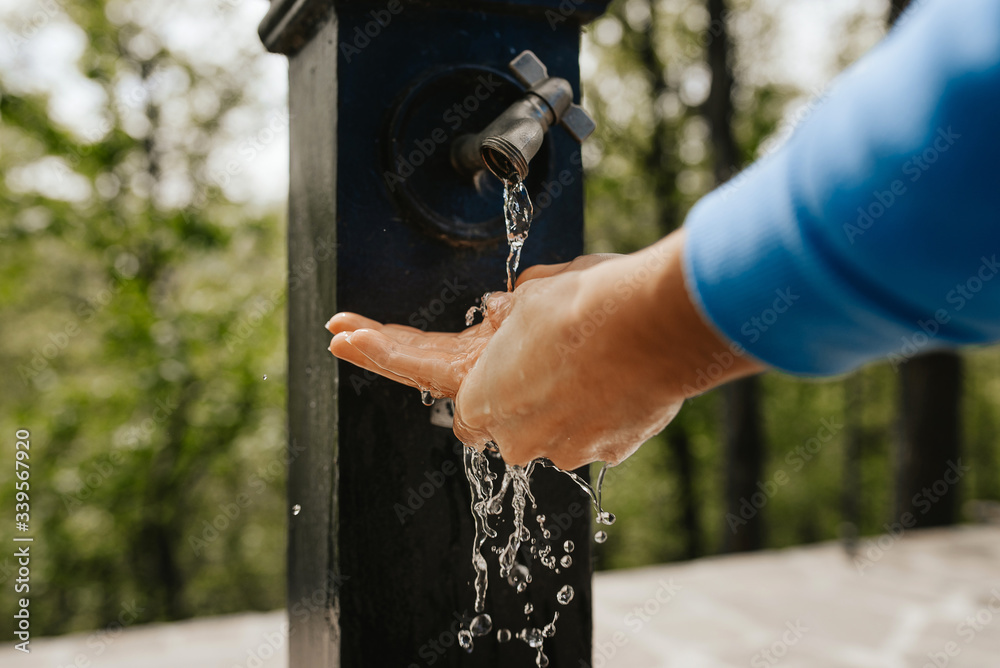 Close up of washing hands under water in a drinking fountain outdoor.