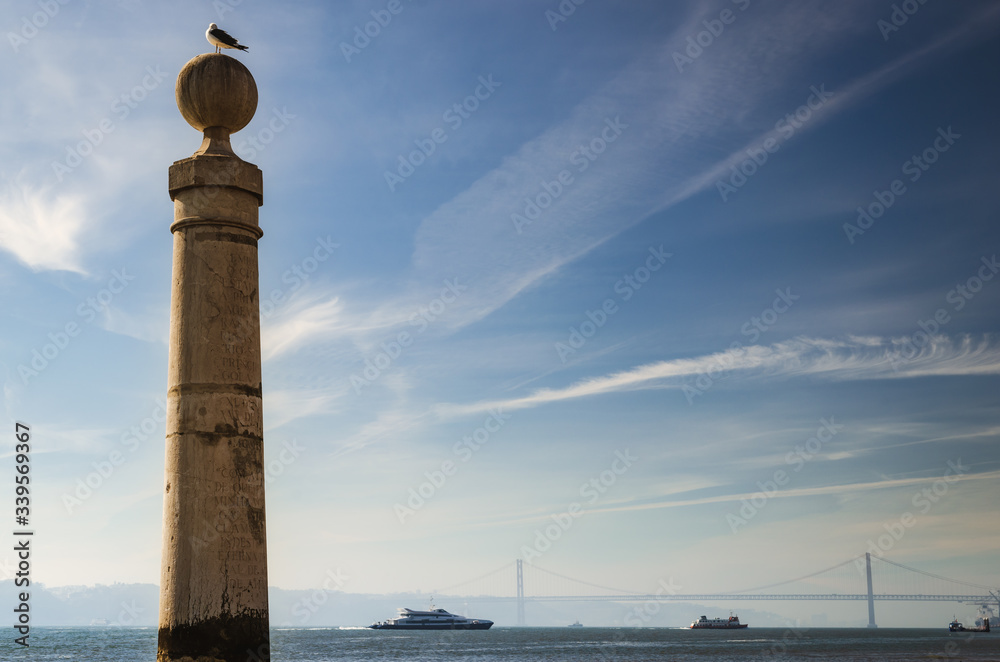 old stone column in the harbor of Praca do Comercio, Lisbon main square, with a seagull looking to the tagus river, the ships and the bridge 25 Abril