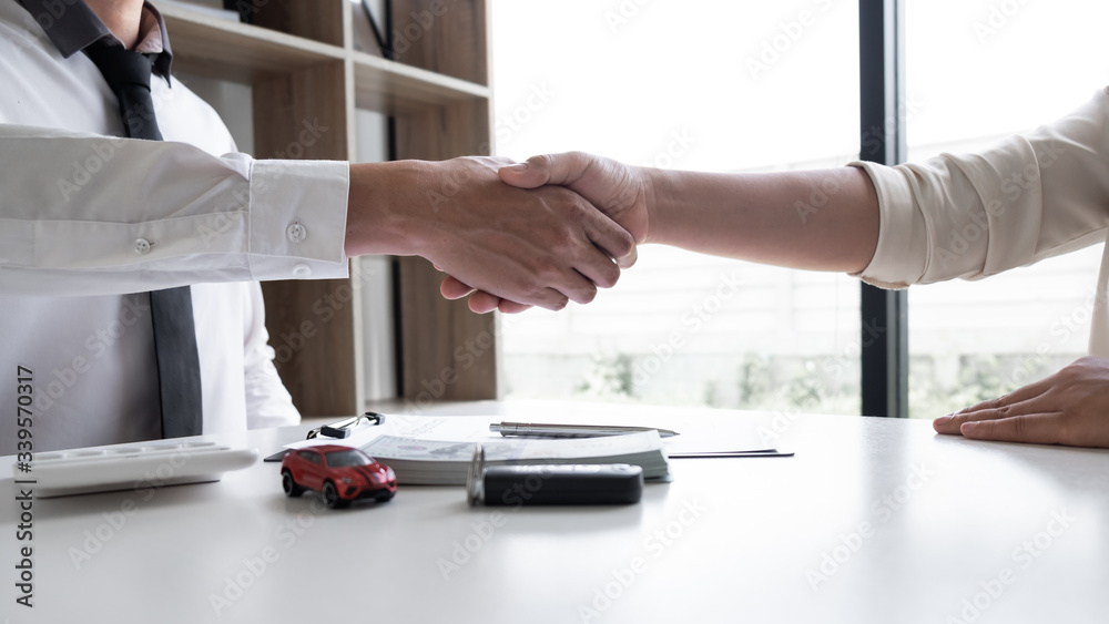 Car sales agent and client shaking hand after finishing signed the car rental agreement in the office.