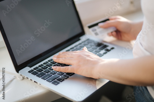 Close up of young woman shopping online using laptop phone and credit card. Laptop on windowsill