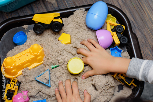 Child playing with kinetic sand and toy construction machinery. Hand of child in sand close up. Flat lay, top view. Indoor Table Game. Creativity Game concept. Activity for fine motor development.