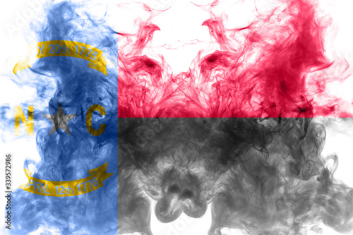 Fototapeta Naklejka Na Ścianę i Meble -  The national flag of the US state North Carolina in against a gray smoke on the day of independence in different colors of blue red and yellow. Political and religious disputes, customs and delivery.
