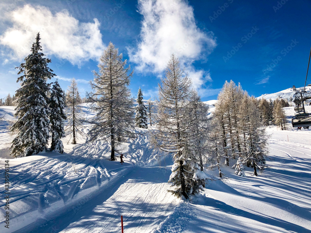 Obraz premium Nassfeld Ski Center with snowed trees and a downhill with some clouds on a blue sky