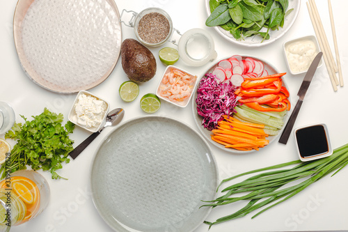 Top view of ingredients for cooking spring rolls with avocado and shrimps, rice paper and soy sauce on a white background.