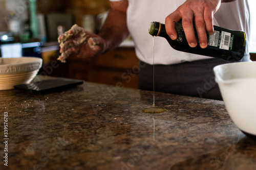 A man pouring olive oil onto a kitchen worktop in preparation to knead bread dough