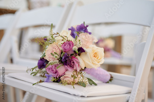 Fototapeta Naklejka Na Ścianę i Meble -  Bridesmaid flower arraignment laying on white ceremony chair for wedding outdoor setting up close