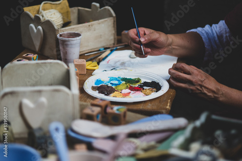 Mani dell'artista femminile che tengono tavolozza sporca sudicia con differenti pitture e pennello nello studio di arte. Stile di vita e concetto di hobby