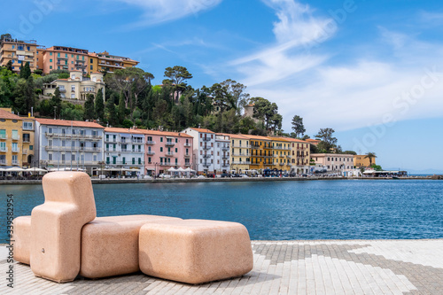 Bench on seafront in Porto Santo Stefano village in a sunny day with beautiful cloudy sky. Grosseto, Tuscany, Italy photo