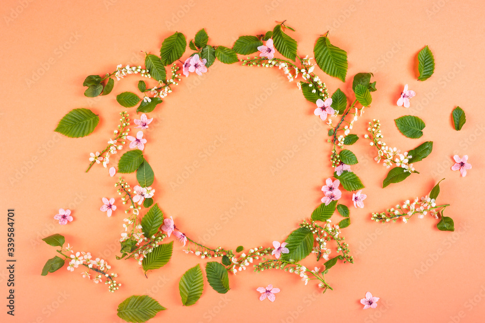 Round frame made of fresh spring texture leaves of different sizes with pink flowers on a bright background. The concept of spring flowering and renewal.