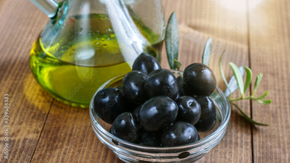 Black canned olives in glass transparent bowl, olive oil bottle in sunlight on the wooden table. Healthy mediterranean food. Black canned olives in glass transparent bowl, olive oil bottle in sunlight on the wooden table. Healthy mediterranean food.