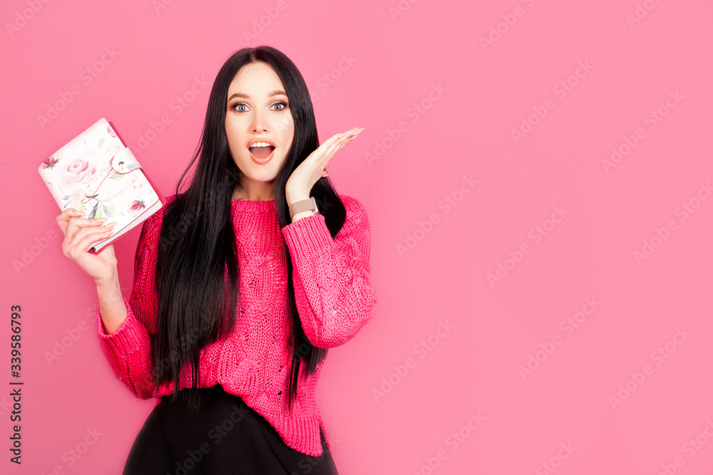 Emotion of strong joy and surprise in a woman with a Notepad on a pink background, with copy space. Concept idea, women's work, planning and business woman Emotion of strong joy and surprise in a woman with a Notepad on a pink background, with copy space. Concept idea, women's work, planning and business woman