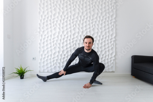 Stretching Instructions. Home fitness. COVID-19 concept. Exercises for all muscle groups. Muscular man demonstrates gymnastic exercises. Stretching inguinal tendons with a lunge on one leg.