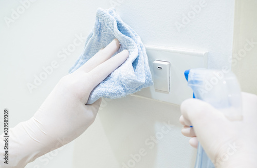Asian women work at home using alcohol spray or antiseptic to clean light switch to prevent spreading of coronavirus during crisis of covid-19. housework, work from home and social distancing concept.