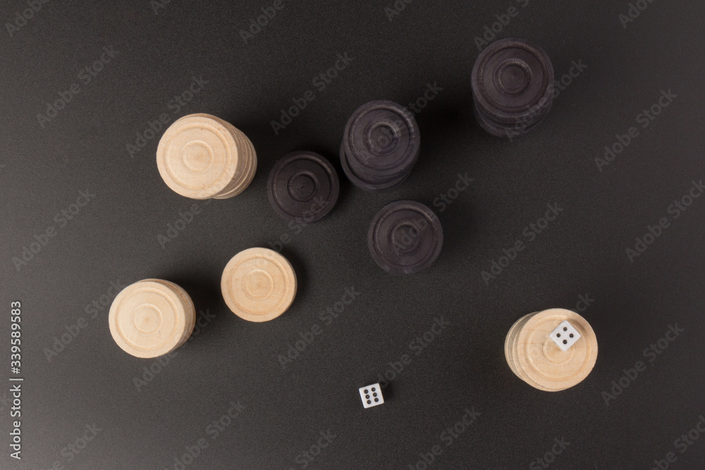 Backgammon. Board game. White dice and white and black chips for playing on a black background. Game for recreation Backgammon. Board game. White dice and white and black chips for playing on a black background. Game for recreation
