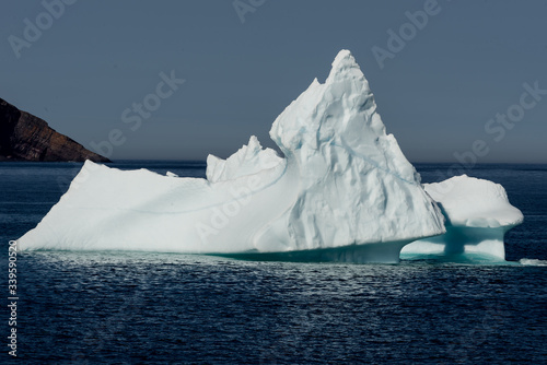 A large glacier iceberg with a high peak in the centre of the berg. The ocean is blue with small waves. The background is grey and foggy. 