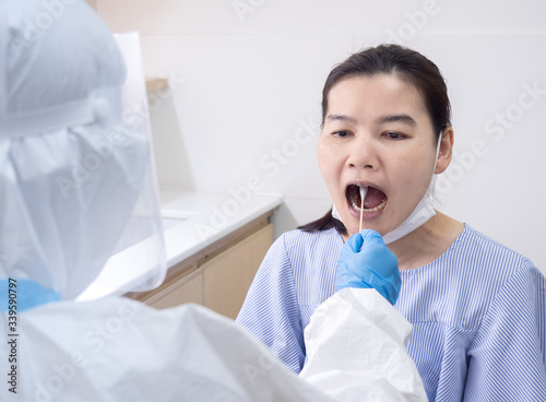 Woman doctor in personal protective suit using cotton swab to do buccal swab sample collection for coronavirus testing from patient at risk of coronavirus infection. Covid-19 and vaccination concept
