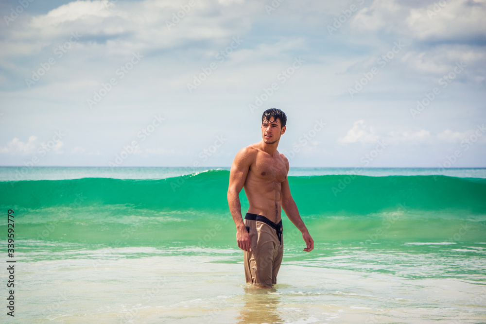 Handsome young man standing on a beach in Phuket Island, Thailand, shirtless wearing boxer shorts, showing muscular fit body