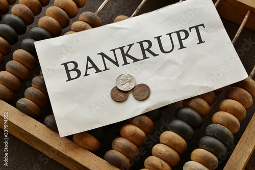 Abacus, coins and a note with the text Bankrupt. The concept of impoverishment and bankruptcy