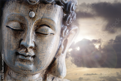 Kopf einer hölzernen Buddha-Figur im Gegenlicht mit Blendenflecken photo