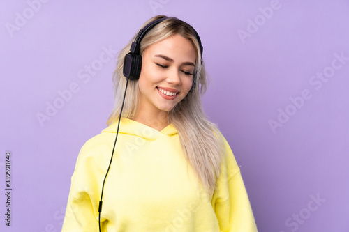 Teenager girl over isolated purple background listening music