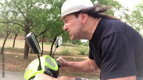 A funny man with a helmet from the pot riding the scooter. The motorcycle race in Asia.