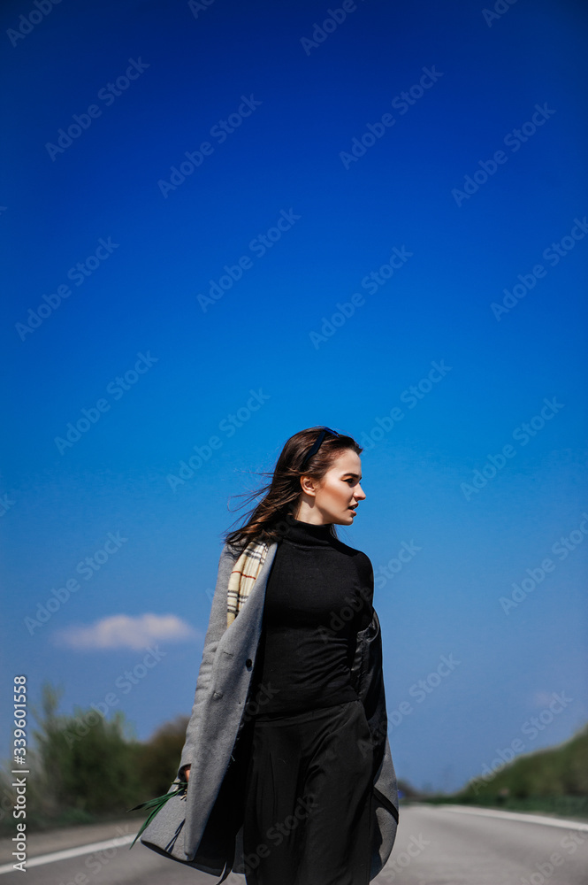 Fashionable attractive young girl posing on the road. Portrait against a clear blue sky Fashionable attractive young girl posing on the road. Portrait against a clear blue sky