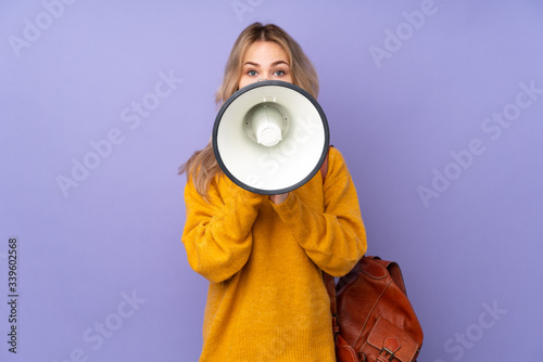 Teenager Russian student girl isolated on purple background shouting through a megaphone