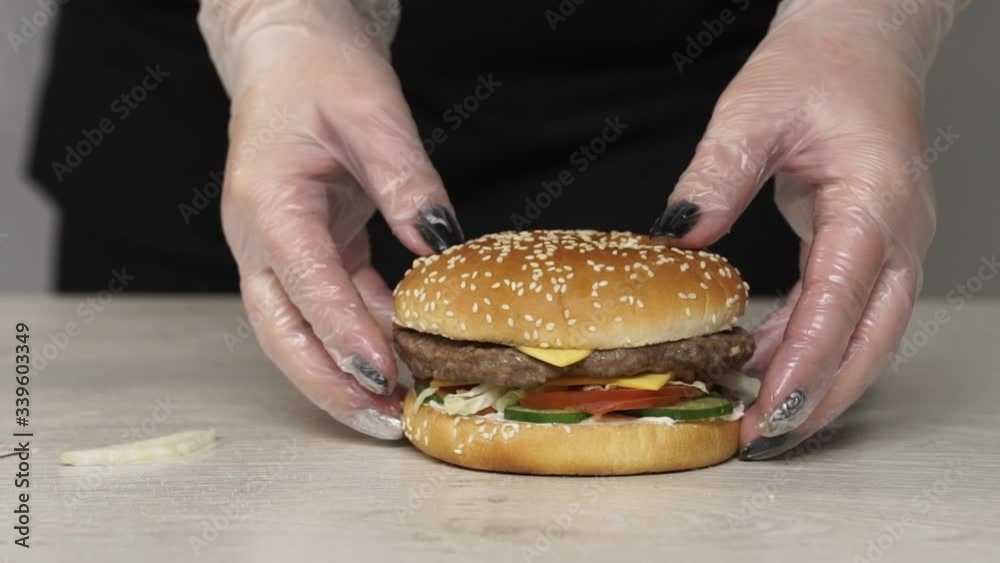 Close up of professional chef cooks a delicious burgers at fast food restaurant. Female chef in gloves finished cooks burger Close up of professional chef cooks a delicious burgers at fast food restaurant. Female chef in gloves finished cooks burger