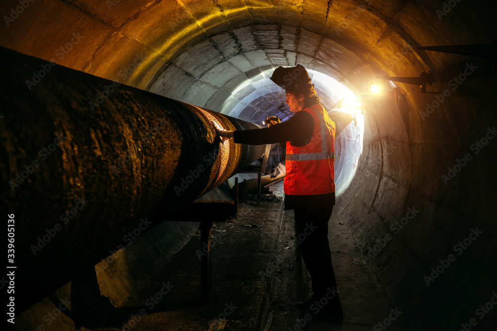 Fototapeta premium Tunnel worker examines pipeline in underground tunnel