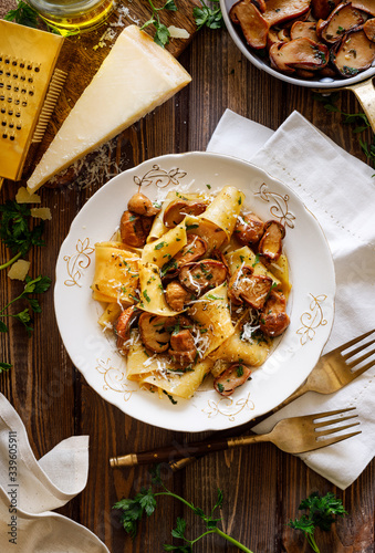 Pappardelle pasta with porcini mushrooms, sprinkled with parmesan cheese and chopped parsley in a ceramic plate on a wooden table, top view. 