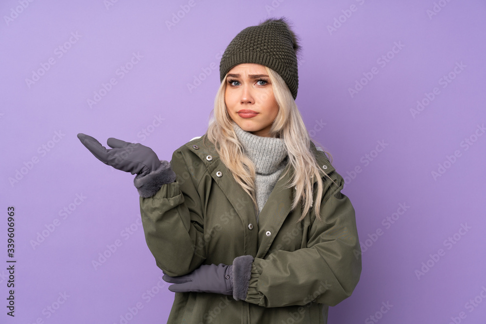 Teenager blonde girl with winter hat over isolated purple background unhappy for not understand something Teenager blonde girl with winter hat over isolated purple background unhappy for not understand something