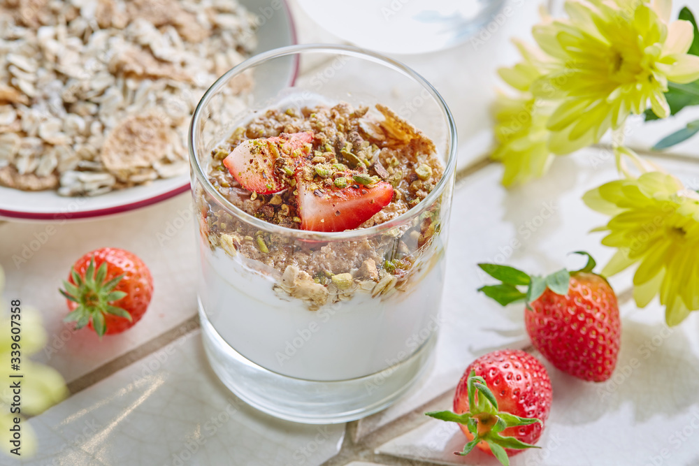 Homemade Granola in glass with yogurt, fresh strawberries, honey and pistachios on white table among yellow flowers. Proper and healthy breakfast. Homemade Granola in glass with yogurt, fresh strawberries, honey and pistachios on white table among yellow flowers. Proper and healthy breakfast.