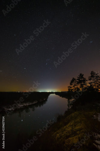 Bright stars of the night sky over the river. Landscape with a view of outer space. © olgapkurguzova