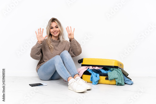 Teenager blonde girl with a suitcase full of clothes sitting on the floor counting nine with fingers photo