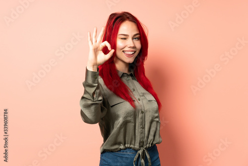 Teenager red hair girl isolated on pink background showing ok sign with fingers