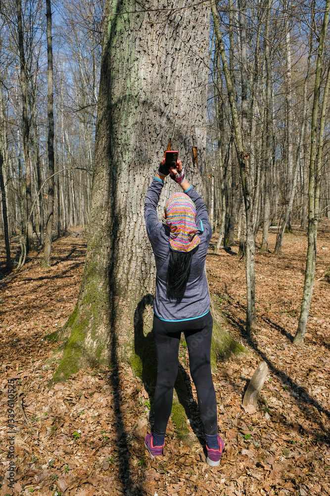 59 year old sporty woman taking pictures of old mighty tree in forest in Ukraine on a sunny day. Back view. 59 year old sporty woman taking pictures of old mighty tree in forest in Ukraine on a sunny day. Back view.