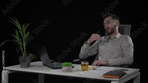 Young attractive bearded male copywriter looking for idea rotating in chair puts on his glasses and starts typing. Indoor studio shot on black background.