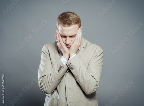 A young man close-up in a suit on a gray background, fall asleep, tired man,stressed and with headachetired man,stressed and with headache. The guy wants to sleep. Gesture. Photos