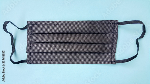 Black face mask on a blue background. Medical item for protection against coronavirus by airborne droplets.