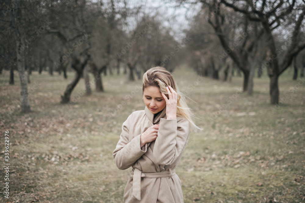 Young beautiful woman in a beige coat walks alone in a park on the street. Resting, windy weather, positive emotions, power balance. Stylish clothes for autumn, spring. Young beautiful woman in a beige coat walks alone in a park on the street. Resting, windy weather, positive emotions, power balance. Stylish clothes for autumn, spring.