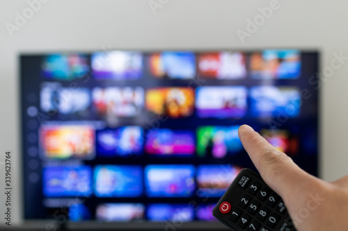Tv remote controller in hand of customer looking for some content in Smart Tv app for streaming video. Watching streaming services for entertainment on television. Choosing TV series and movies
