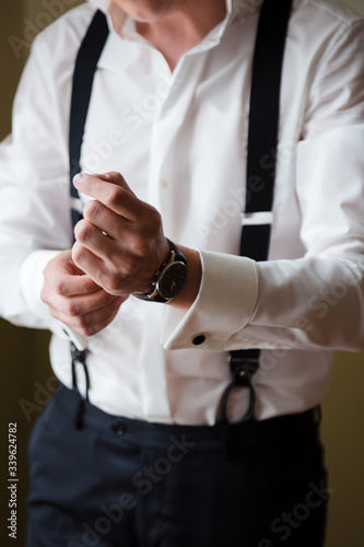 Groom's morning. A man in a white shirt and suspenders puts a watch on his wrist. Close up, no face. Preparation for the wedding