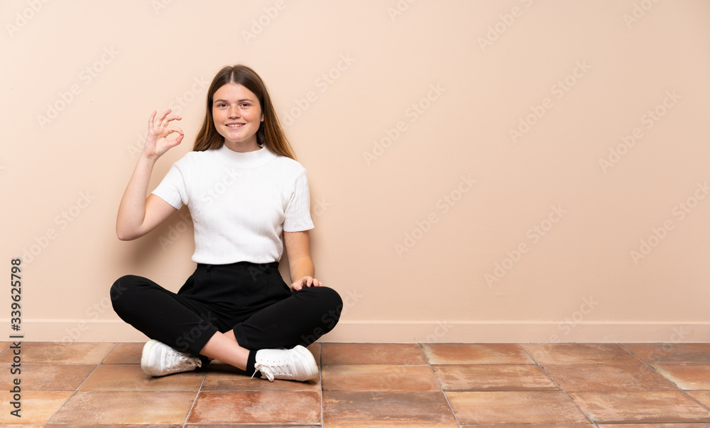 Ukrainian teenager girl sitting on the floor showing ok sign with fingers Ukrainian teenager girl sitting on the floor showing ok sign with fingers