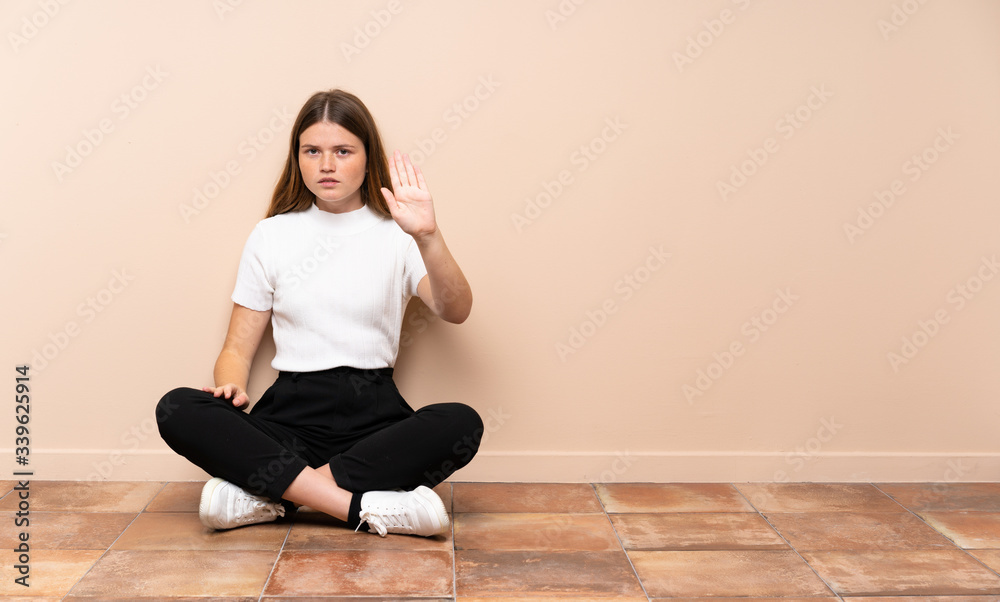 Ukrainian teenager girl sitting on the floor making stop gesture Ukrainian teenager girl sitting on the floor making stop gesture